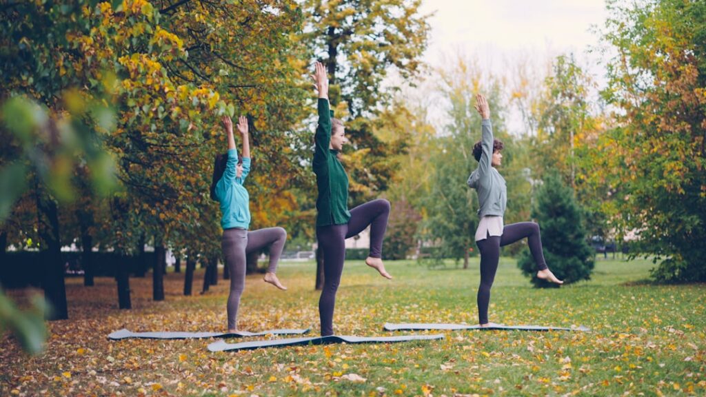 Three people practicing yoga in an autumn park.