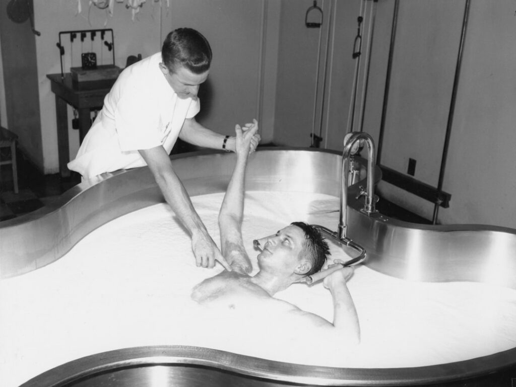 Therapist assists patient in a large hydrotherapy tub.