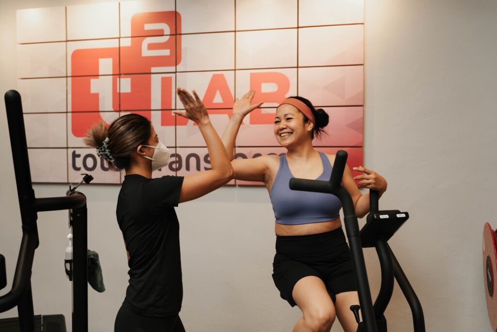 Two women high-fiving while exercising on machines